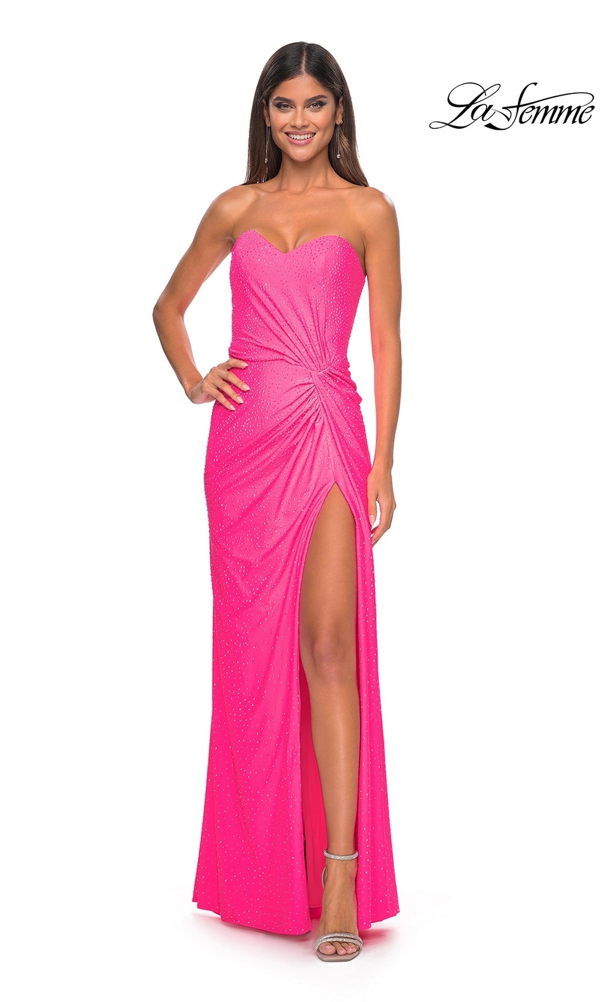 A woman smiles in the La Femme Twist Strapless Long Prom Dress 32175—bright pink, long, with a high slit, subtle embellishments, and ruched waist detailing for an elegant look.